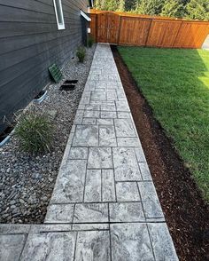 a walkway made out of pavers next to a house with a wooden fence in the background