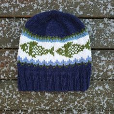 a blue and white knitted hat sitting on top of a wooden bench with snow flakes