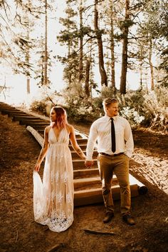 a man and woman are walking down some steps in the woods holding each other's hands