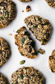 several cookies with nuts and seeds are on a white tablecloth next to each other