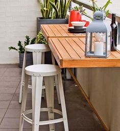 a wooden table topped with white stools next to a potted plant and bottle