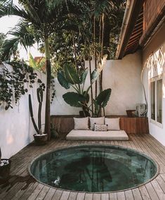 a small pool in the middle of a wooden deck next to a house with plants