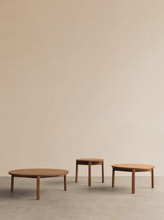 three wooden tables sitting next to each other on top of a cement floor in front of a beige wall