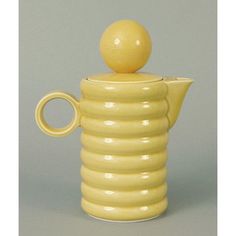 a yellow ceramic tea pot with a ball on the top, sitting in front of a gray background