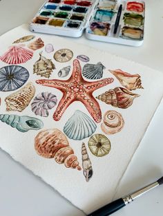 a watercolor painting of seashells and starfish on white paper with paintbrushes next to it