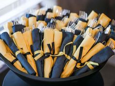 there are many forks and knives in the black bowl with yellow ribbons on it's sides