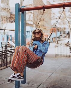 a woman is sitting on a swing in the park while wearing sunglasses and striped pants