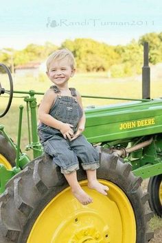 a little boy sitting on the back of a green and yellow tractor in a field