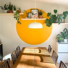 a dining room table with plants and pictures on the wall above it in front of a yellow circle