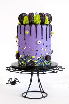 a purple cake with sprinkles and decorations on a black stand against a white background