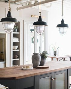 a kitchen island with two vases on it and lights hanging from the ceiling above