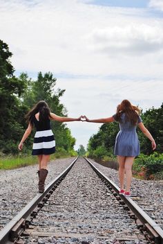 two girls walking on railroad tracks holding hands