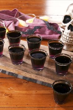 a wooden table topped with shot glasses filled with dark colored liquid next to a skull