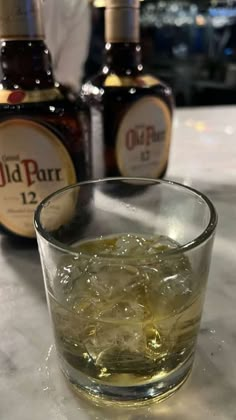 a glass filled with ice sitting on top of a table next to two bottles of alcohol