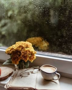 a cup of coffee sitting on top of a window sill next to an open book