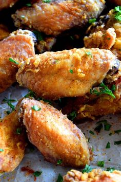 fried chicken wings with parsley and seasoning sitting on top of parchmented paper