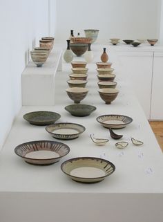 several bowls and plates are on display in a room with white walls, flooring and wooden floors