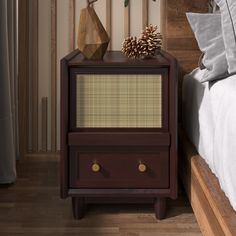 a night stand with two drawers and pine cones on top, in front of a bed