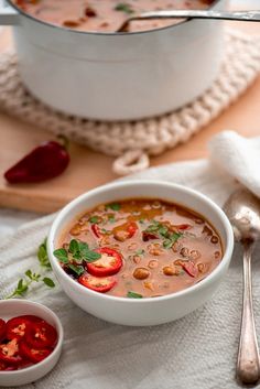 there is a bowl of soup on the table with silverware and spoons next to it