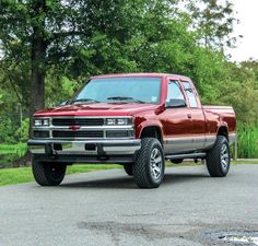 a red pick up truck parked on the side of a road next to some trees