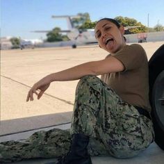 a woman sitting on the ground with her tongue out and an airplane in the background