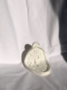 a white ceramic clock sitting on top of a white cloth covered table next to a person's shadow