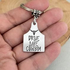 a hand holding a metal keychain that says drive safe cowboy