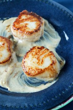 three scallops are sitting on top of some cream sauce in a blue bowl