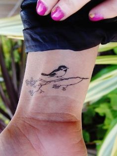 a woman's wrist with a small bird on top of the tree branch tattoo