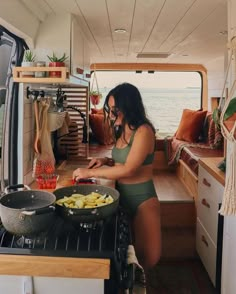 a woman in a green bathing suit cooking food inside of a camper with the door open