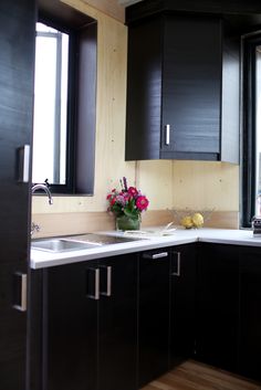 a kitchen with black cabinets and white counter tops is pictured in this image, there are flowers on the counter