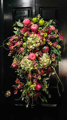 a bunch of flowers hanging from the side of a black door with green and red leaves