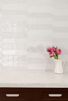 a vase with pink flowers sitting on top of a white counter next to a wooden cabinet