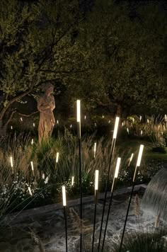 some lights are lit up in the dark near a water fountain and statue at night