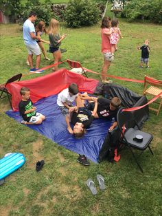 a group of people sitting on top of a blue and red tarp in the grass