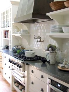 a kitchen with white cabinets, black counter tops and stainless steel range hood over the stove