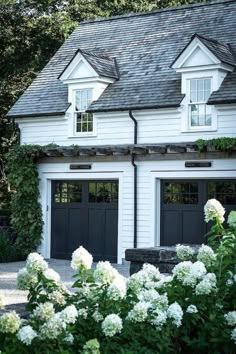 two garages with black doors and windows in front of some white hydrangeas