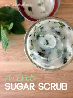 two glasses filled with mint sugar scrub on top of a wooden table next to green leaves