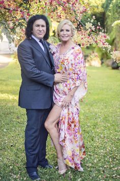 a man and woman standing in front of a tree with pink flowers on the branches