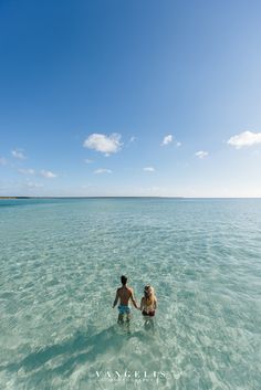 two people are holding hands in the water on a sunny day with blue skies above them