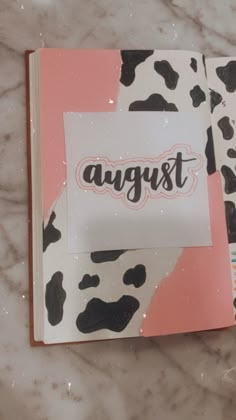 an open notebook with the word august written in black and white on it, sitting on a marble surface