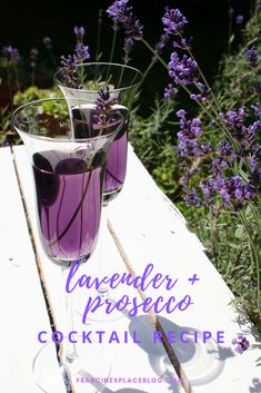 two glasses filled with purple liquid sitting on top of a wooden table next to lavender flowers