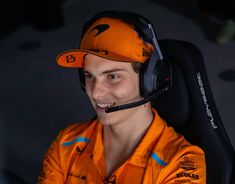 a man in an orange shirt and headphones smiles at the camera while wearing a headset