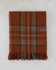 a brown plaid scarf with fringes on a marble surface, showing the end of it