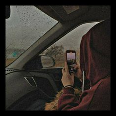 a person sitting in a car holding a cell phone up to their face and looking at the screen