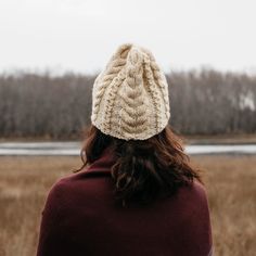 a woman wearing a white knitted hat looking out over an open field with trees in the background