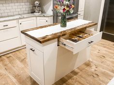 a kitchen with white cabinets and wooden counter tops, an open drawer in the center