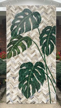 a painting with green leaves on it in front of a brick wall and potted plants