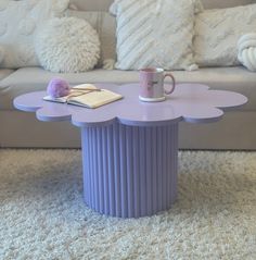 a purple table with a book and coffee cup on it in front of a couch