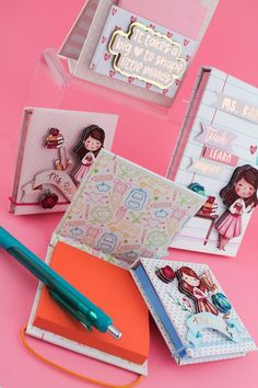 three small notebooks and a pen on a pink surface with greeting cards in the background